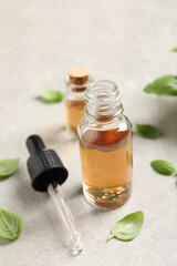 Bottles of essential basil oil and fresh leaves on light grey table