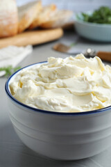 Bowl of tasty cream cheese on grey table, closeup