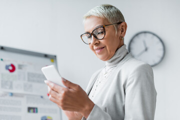 pleased senior businesswoman in glasses looking at smartphone