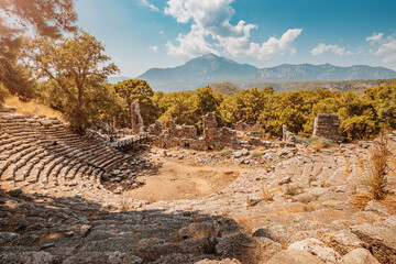 Fototapeta na wymiar Ruins of an antique Greek amphitheater in the ancient city of Phaselis in present-day Turkey with Tahtali mountains in the background. Sightseeing and travel
