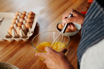 Hands of multi-cultural elderly female whisking eggs in a glass bowl. Retired, cooking healthy breakfast at home.