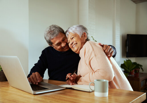 Multi-cultural elderly couple celebrating after receiving good news. Sitting at modern kitchen counter with laptop. - Powered by Adobe