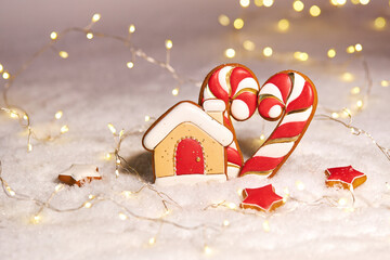 A heart made of gingerbread candy cane shaped cookies with a gingerbread house  on a white snowy background. Valentine's day background
