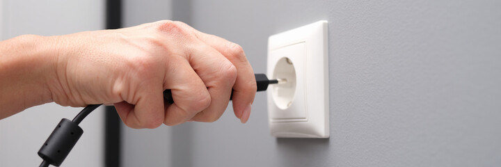 Woman hand inserts an electrical plug into outlet closeup