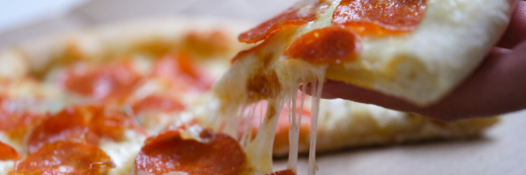 Woman holding piece of delicious hot pizza over box closeup