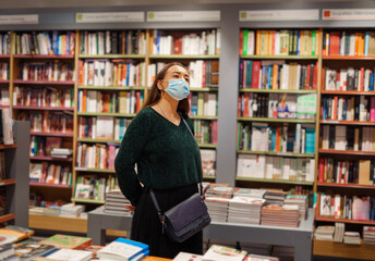 Young lady in face mask stands in bookstore during covid19 outbreak