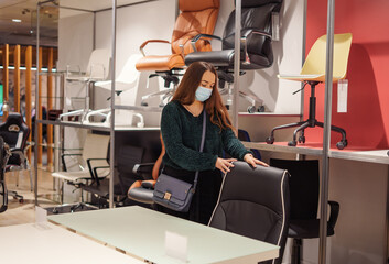 Young woman in white face protective mask choosing office furniture during covid-19 pandemic