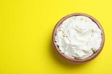 Bowl of tasty cream cheese on yellow background, top view. Space for text