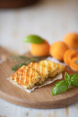 Slices of fried halloumi cheese with a beautiful grilling pattern rests on a wooden tray with apricot slices.