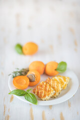 Slices of fried halloumi cheese with a beautiful grilling pattern rests on a white plate with apricots.