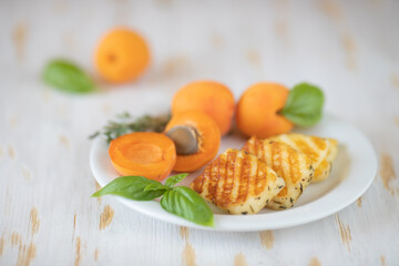 Slices of fried halloumi cheese with a beautiful grilling pattern rests on a white plate with apricots.