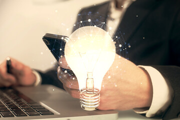 Double exposure of man's hands holding and using a digital device and bulb hologram drawing. Idea concept.