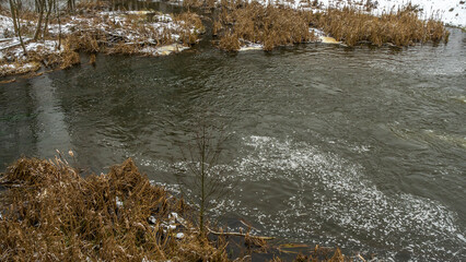 Winter landscape of a small river in early winter on a cloudy day. River dry grass in the crystals.