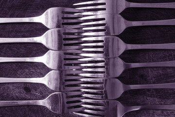 Several shiny metal forks lie with overlapping teeth on a cutting board. Background. Texture. Monochrome.