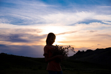 Silhouette of a girl with a bouquet of flowers on the background of a sunset in the mountains. The concept of summer fun