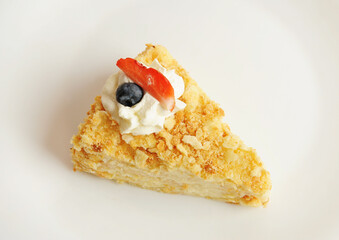 Slice of classic Napoleon cake decorated with cream and berries on white plate
