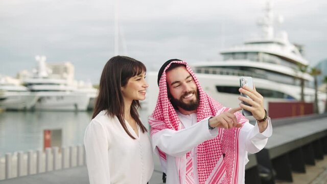 Smiling arab businessman taking selfie with his beautiful caucasian female assistant in port