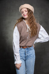 Beautiful girl model with long hair in a beige beret and jeans posing on a gray background.