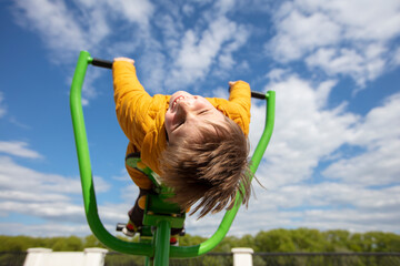Funny little boy on a swing with his head down. Happy child for a walk. Ten year old boy against...