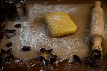 The dough lies on parchment next to a rolling pin and cookie cutters, flour is scattered everywhere, the photo is in dark colors. High quality photo