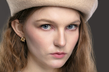 The face of a girl in a beret on a gray background.