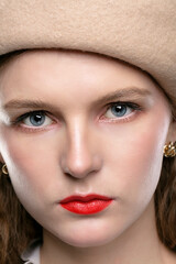 Close up portrait of a young beautiful woman in a beige beret and red lips.