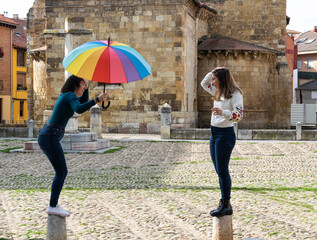 Dos chicas jovenes y divertidas haciendo payasadas en la calle mientras juegan con un paraguas multicolor arcoiris