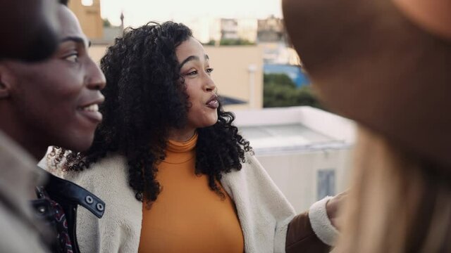 Mixed race female and multi-ethnic group of adult friends socializing on a rooftop in the city at dusk
