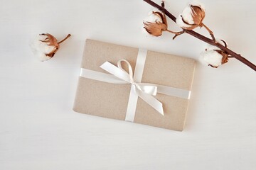 Gift package wrapped with brown paper and white ribbon, cotton branches as decoration, mockup for gift label or sticker presentation.