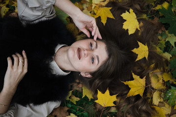 beautiful pose in autumn leaves. the girl lies on yellow leaves. leaves adorn the hair. blue eyes look up to the sky. the girl touches her face with her hand.