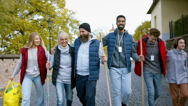 Diverse group of happy volunteers walking with tools to do street clean up, community service concept