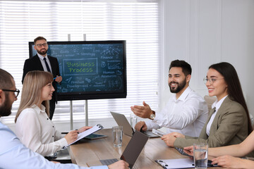 Business trainer near interactive board in meeting room during presentation, focus on colleagues