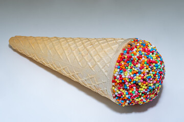 Ice cream cone with little cup cake decorated with frosting and round sprinkles with sprinkles...