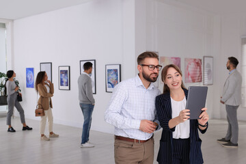 Happy couple with tablet at exhibition in art gallery