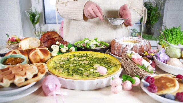 Woman prepare festive dinner, Easter brunch. Traditional Easter dishes on family home table - baked meat, quiche, spring salad, muffin, colored eggs, hot cross buns
