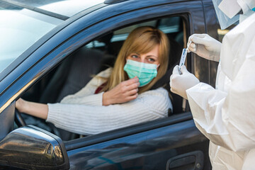 Woman sitting in car, waiting for medical worker in PPE to perform drive-thru COVID-19 test