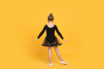 Fototapeta na wymiar Cute little girl in black dress dancing on yellow background, back view