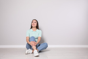 Fototapeta premium Young woman sitting on floor near light grey wall indoors. Space for text