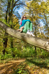 Fototapeta na wymiar Little girl climbed on tree. Girl sitting in a tree in an autumn forest