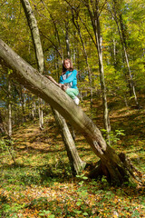 Naklejka na ściany i meble Little girl climbed on tree. Girl sitting in a tree in an autumn forest