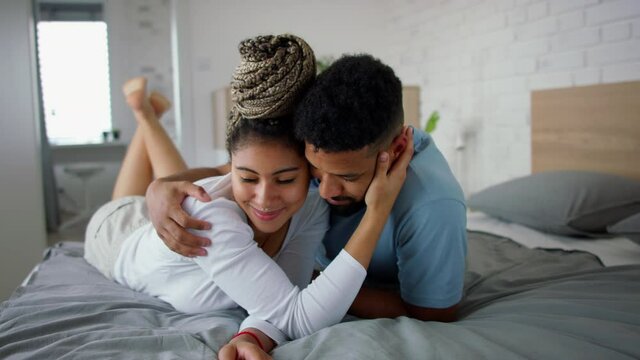 Multiracial young couple in love lying on bed and cuddling together indoors at home.