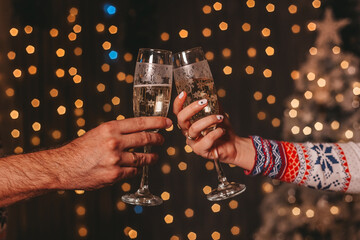 Two lovers drinking champagne on the background of golden lights. Couple toasting wineglasses in a luxury restaurant. Focus on the wineglass