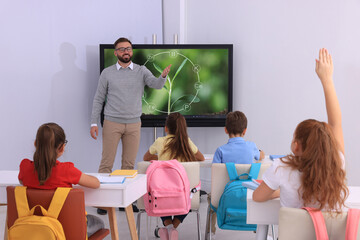 Teacher giving lesson to pupils near interactive board in classroom