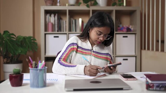 Focused Black Girl with eyeglasses uses calculator and Writes Notes studying for the University College Exams at home
