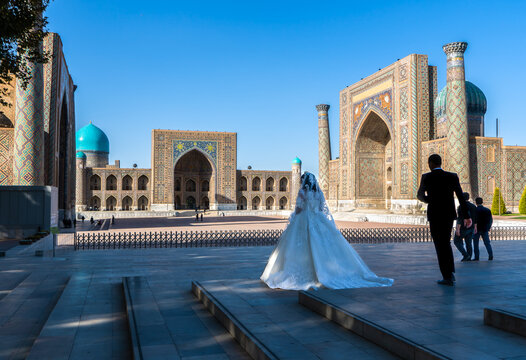 Uzbekistan, Samarkand  wedding couple in traditional clothes posing in front of famous Registan Square. 
