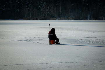 winter fishing. a fisherman is sitting on a frozen lake and fishing in a hole in the ice. winter winter sports winter fishing