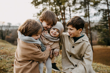 Brothers hugging little sister, smiling, spending time outdoors in a park on autumn day.