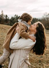 Mother holding her son in arms outdoors, smiling.