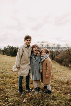 Three brothers hugging, smiling, spending time outdoors in a park on autumn day.