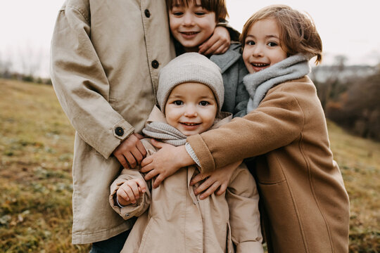 Closeup Of Brothers Hugging Little Sister, Smiling, Outdoors On Autumn Day.